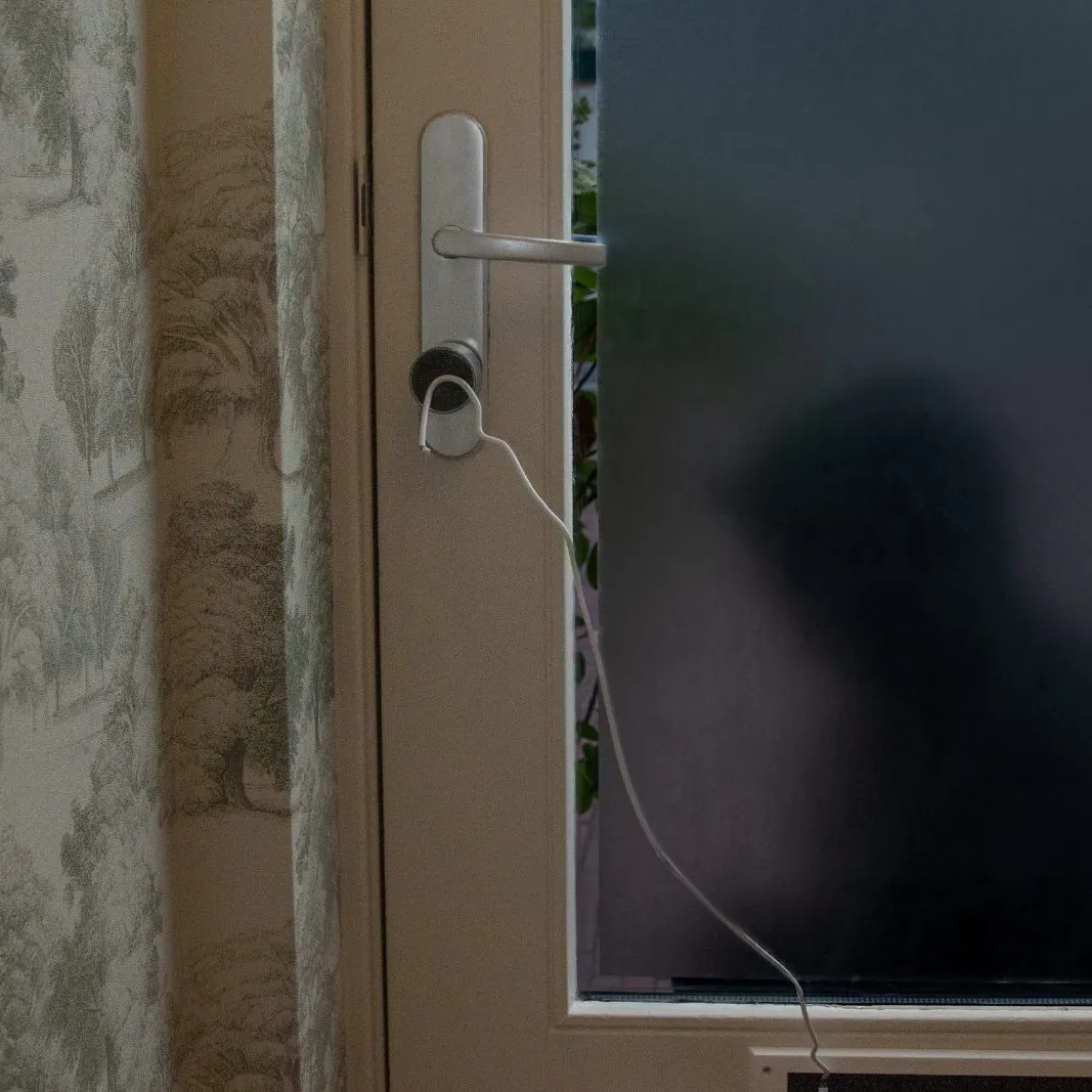 A wire fished around a door’s inside knob, a figure silhouetted through the glass behind it