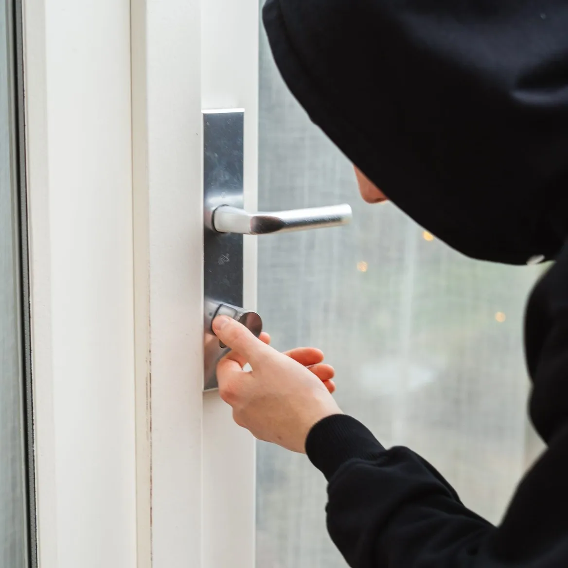 A hooded figure reaching for the cylinder of a front door